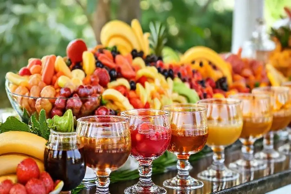 Um buffet de saladas de frutas com caldas variadas em frascos elegantes.