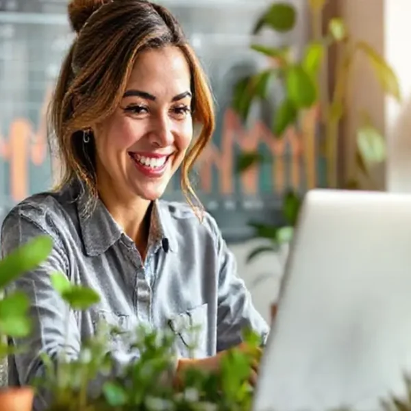Uma mulher sorrindo enquanto trabalha em seu laptop, refletindo prosperidade.