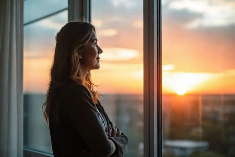 Mulher olhando pela janela com um sorriso, simbolizando um futuro financeiro otimista.