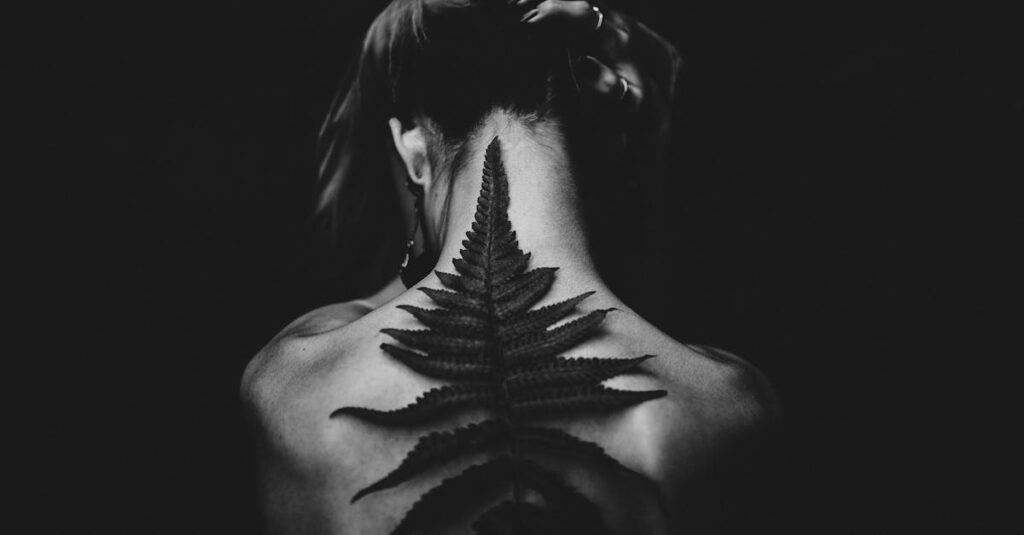 Black and white photo of a tattooed woman from the back, featuring a fern design. Captivating and artistic pose.