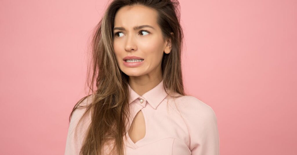 A young woman with a playful uncertain expression against a pink background.