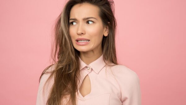 A young woman with a playful uncertain expression against a pink background.