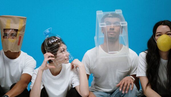 Four people wearing humorous DIY face masks against a blue background, showcasing creativity and humor.