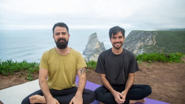 Two men practicing yoga outdoors with scenic ocean views in Portugal.