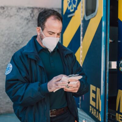 Paramedic in mask working next to EMS vehicle, preparing for emergency response.