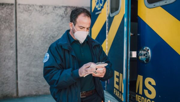 Paramedic in mask working next to EMS vehicle, preparing for emergency response.