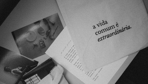 Monochrome still life featuring Portuguese text 'a vida comum é extraordinária' on paper.