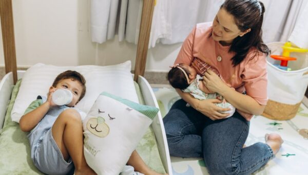 Mother with baby and young child in a warm, nurturing nursery environment.