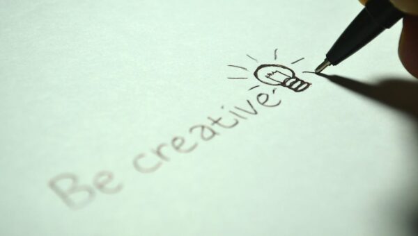 Close-up of handwritten 'Be creative' with a light bulb sketch on paper.
