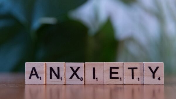 Close-up of wooden blocks spelling ANXIETY on a wooden surface with blurred green background.