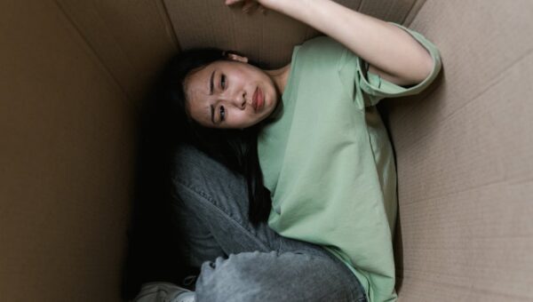 Woman enclosed in a cardboard box, showing signs of stress and fear.