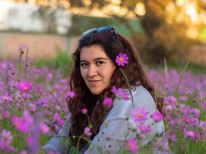 A serene portrait of a woman sitting in a field of pink flowers in Lerma, Mexico, at sunset.