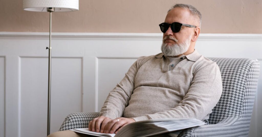 Senior man with sunglasses reading a braille book in a cozy modern interior.