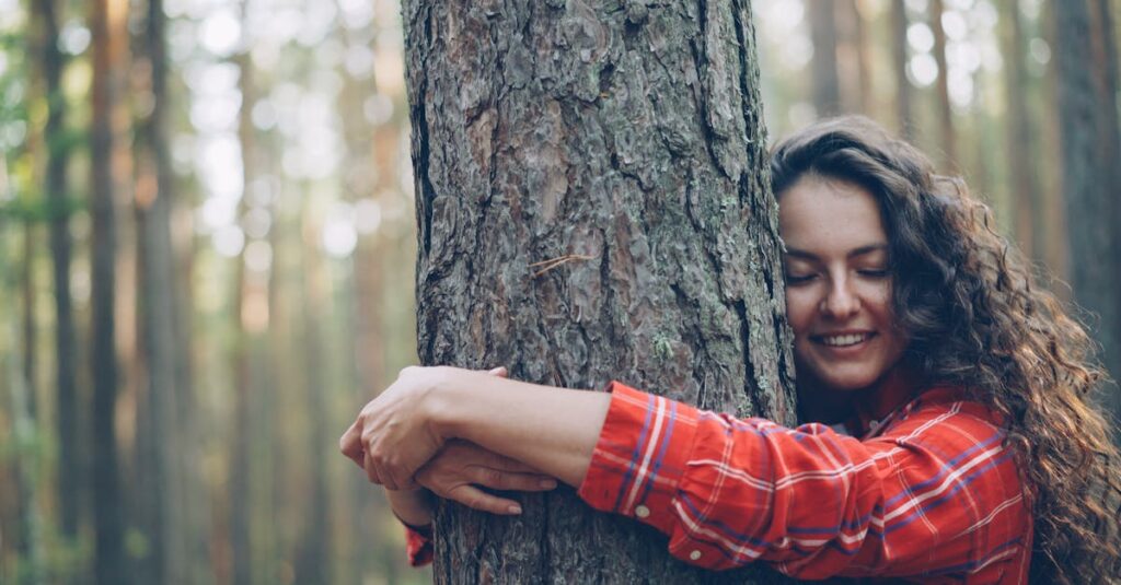 Smiling woman embracing a tree in a sunlit forest, promoting nature connection.