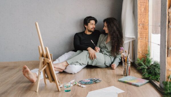 Happy couple sitting on the floor inside, enjoying a painting session with natural light.