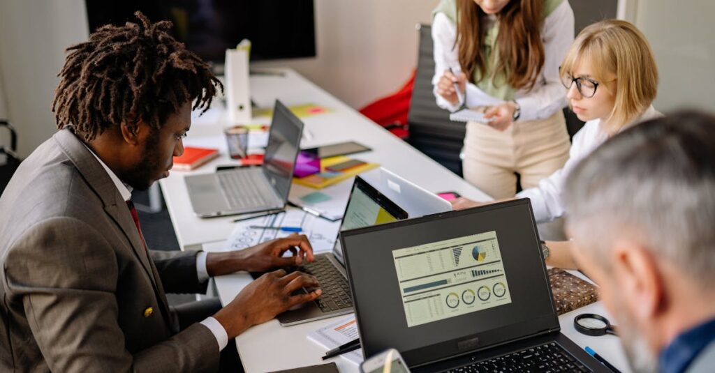 Diverse coworkers engaged in teamwork using laptops and digital devices in a modern office setting.