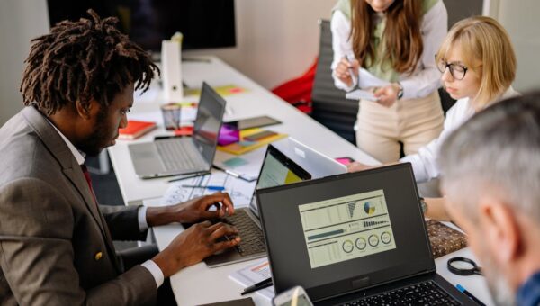 Diverse coworkers engaged in teamwork using laptops and digital devices in a modern office setting.