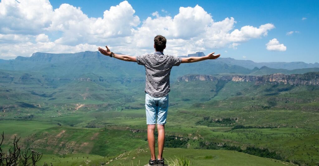 5 Dicas para Cultivar a Autoestima em Momentos Difíceis 2 A man stands triumphantly with arms open, overlooking a scenic mountain range.