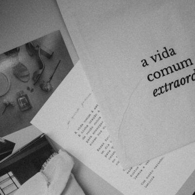 Monochrome still life featuring Portuguese text 'a vida comum é extraordinária' on paper.