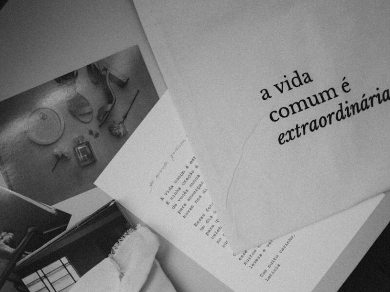 Monochrome still life featuring Portuguese text 'a vida comum é extraordinária' on paper.