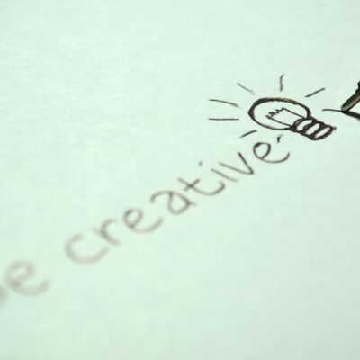 Close-up of handwritten 'Be creative' with a light bulb sketch on paper.
