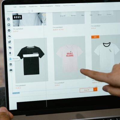 A person points to t-shirt options in an online store on a laptop screen.