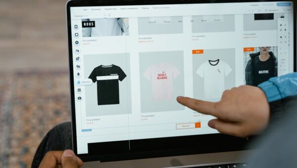 A person points to t-shirt options in an online store on a laptop screen.