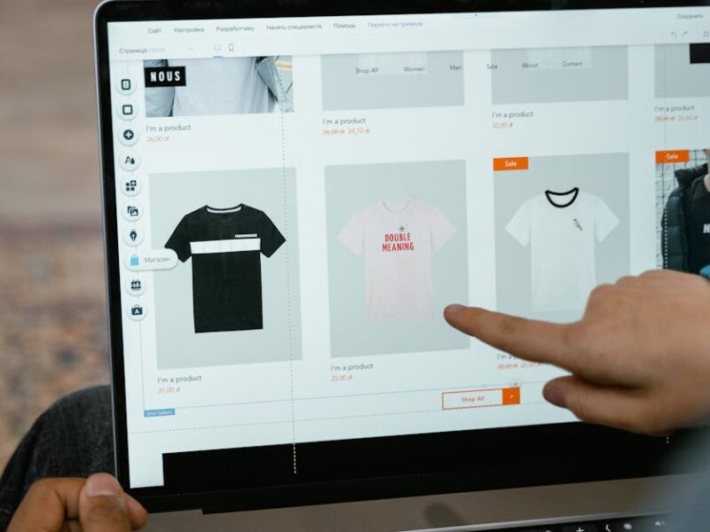 A person points to t-shirt options in an online store on a laptop screen.