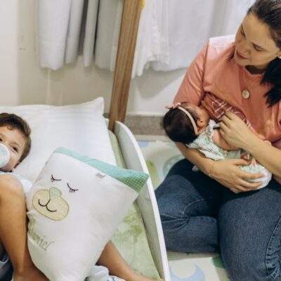 Mother with baby and young child in a warm, nurturing nursery environment.