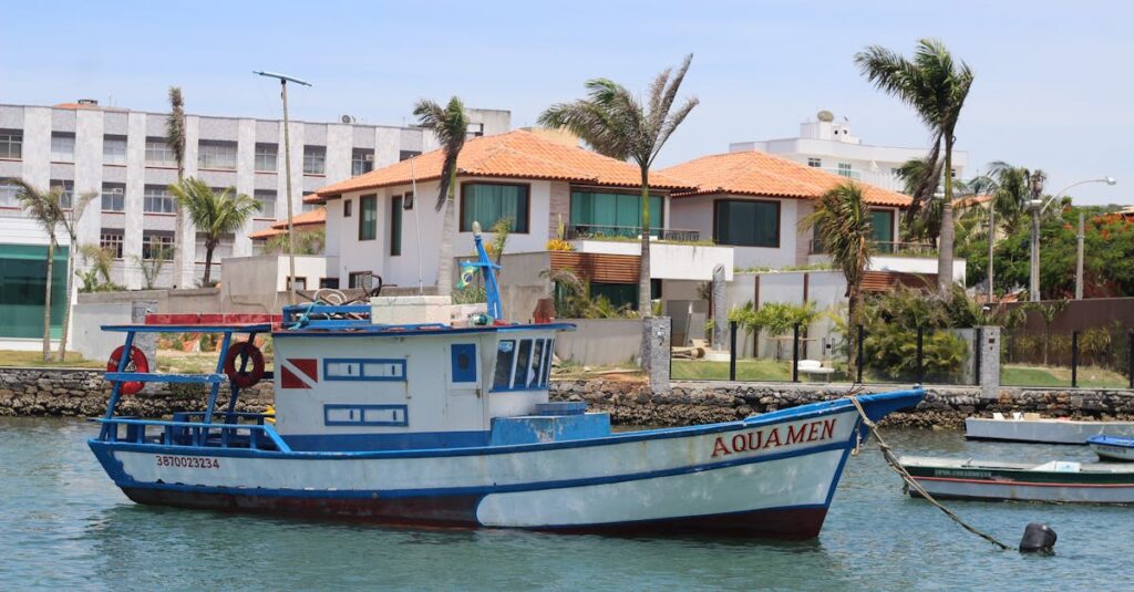 7 Dicas para Viajar Sozinha e se Sentir Empoderada 2 Fishing boat 'Aquamen' docked at a picturesque coastal harbor with palm trees and residences in the background.