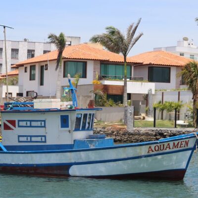Fishing boat 'Aquamen' docked at a picturesque coastal harbor with palm trees and residences in the background.