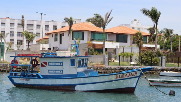 Fishing boat 'Aquamen' docked at a picturesque coastal harbor with palm trees and residences in the background.