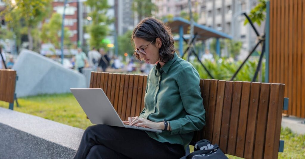 A woman using a laptop on a bench in a city park, embracing remote work outdoors.
