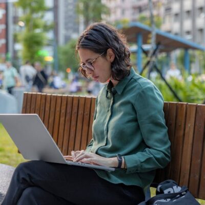 A woman using a laptop on a bench in a city park, embracing remote work outdoors.