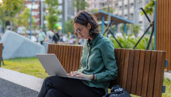 A woman using a laptop on a bench in a city park, embracing remote work outdoors.
