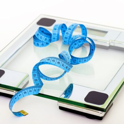 A digital glass weighing scale with a blue measuring tape, symbolizing weight management.