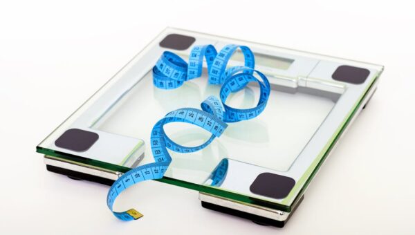 A digital glass weighing scale with a blue measuring tape, symbolizing weight management.