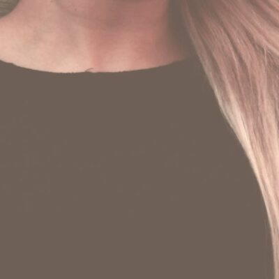 Close-up portrait of a woman with long, flowing blonde hair against a textured background.