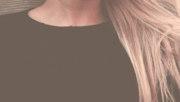 Close-up portrait of a woman with long, flowing blonde hair against a textured background.