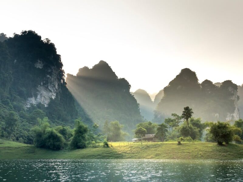 Spectacular scenery of sunlight shining through massive limestone mountains covered with lush green vegetation surrounding ripping lake in Vietnam