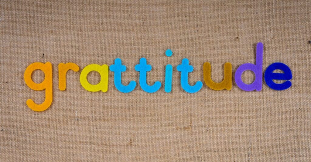 Vibrant colored letters spelling 'gratitude' on a textured burlap surface.