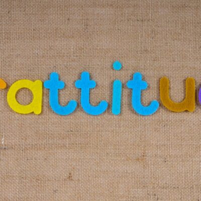 Vibrant colored letters spelling 'gratitude' on a textured burlap surface.