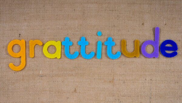 Vibrant colored letters spelling 'gratitude' on a textured burlap surface.