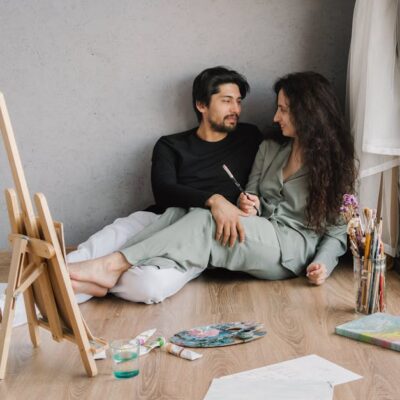 Happy couple sitting on the floor inside, enjoying a painting session with natural light.