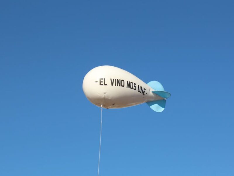 A white balloon with 'El Vino Nos Une' phrase floats against a clear blue sky.