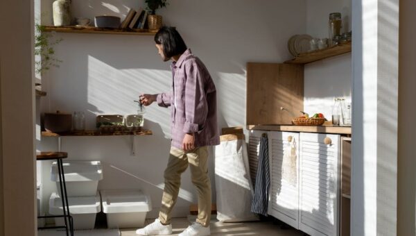 Man in casual wear tending to indoor plants in a sunlit kitchen.