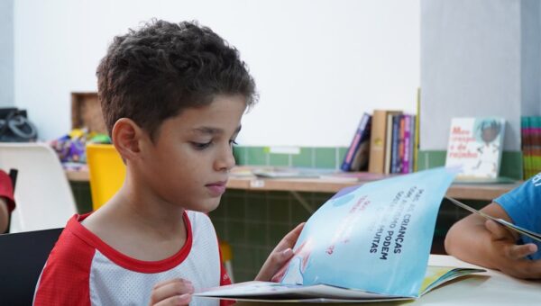 A young boy engrossed in reading a book in a classroom environment, promoting child literacy.