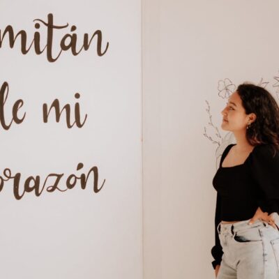 A woman in a black top and denim jeans admires a wall with 'Comitán de mi Corazón' text.
