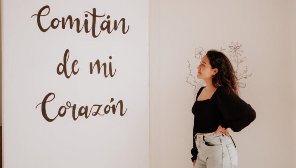 A woman in a black top and denim jeans admires a wall with 'Comitán de mi Corazón' text.