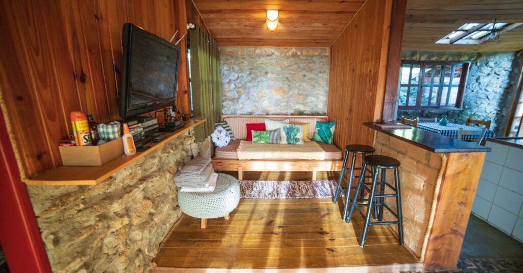 Interior of rustic house with counter placed near sofa with cushions and TV hanging on wooden wall near various supplies